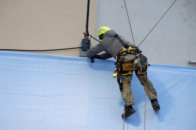 Rope access technician on dual ropes and a full harness working against a large surface