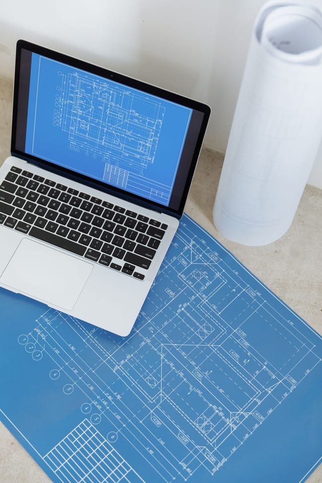 Laptop showing a technical drawing beside rolled engineering plans