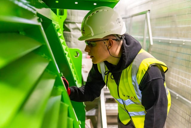 Technician in hi-vis and hard hat inspecting a steel structure at an industrial plant