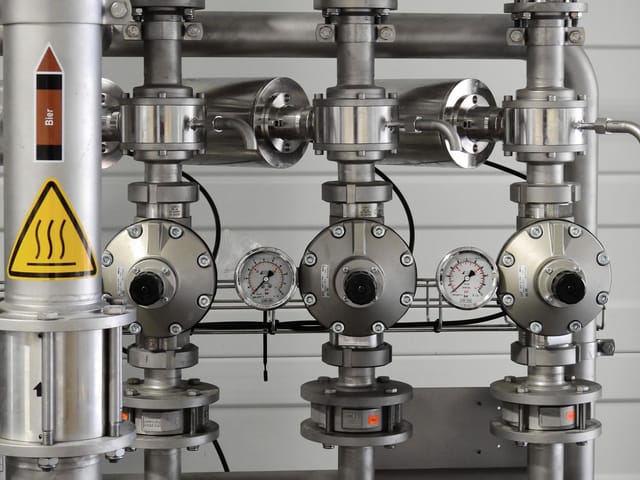 Flanged process valves with pressure gauges and a hot surface warning on plant