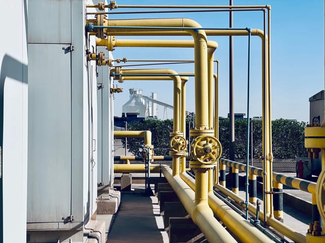 Process pipework and a walkway running through an industrial plant against a clear sky
