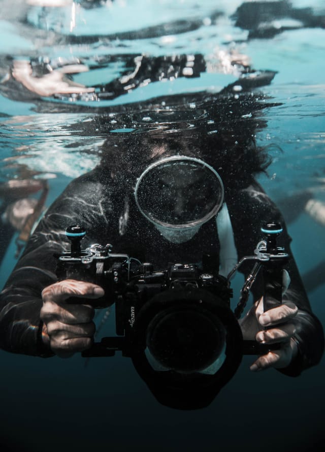 Operator in the water controlling a tethered underwater camera on an umbilical