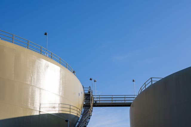 A large above ground storage tank with an access walkway against a clear sky