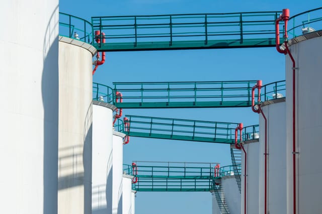 White storage tanks with access walkways under a clear blue sky