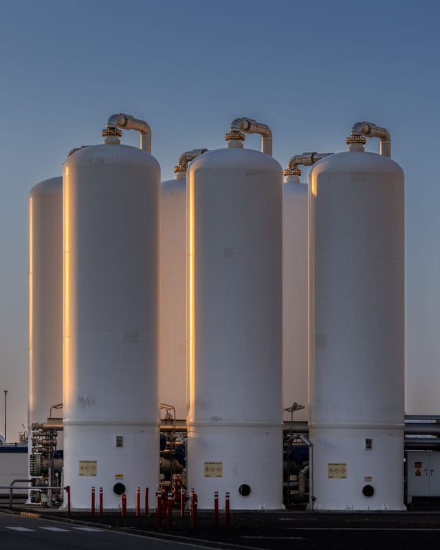 A row of pale plastic and composite storage vessels against a clear sky