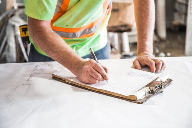Engineer in hi-vis marking up technical drawings on a clipboard at a work table