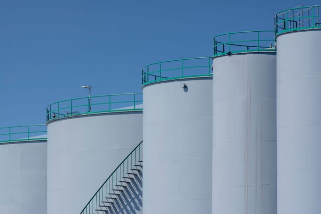 A row of white pressure vessels and storage vessels with access stairways against a clear sky