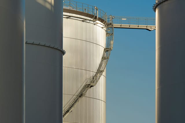 A large vertical pressure vessel with a spiral access stairway against a blue sky